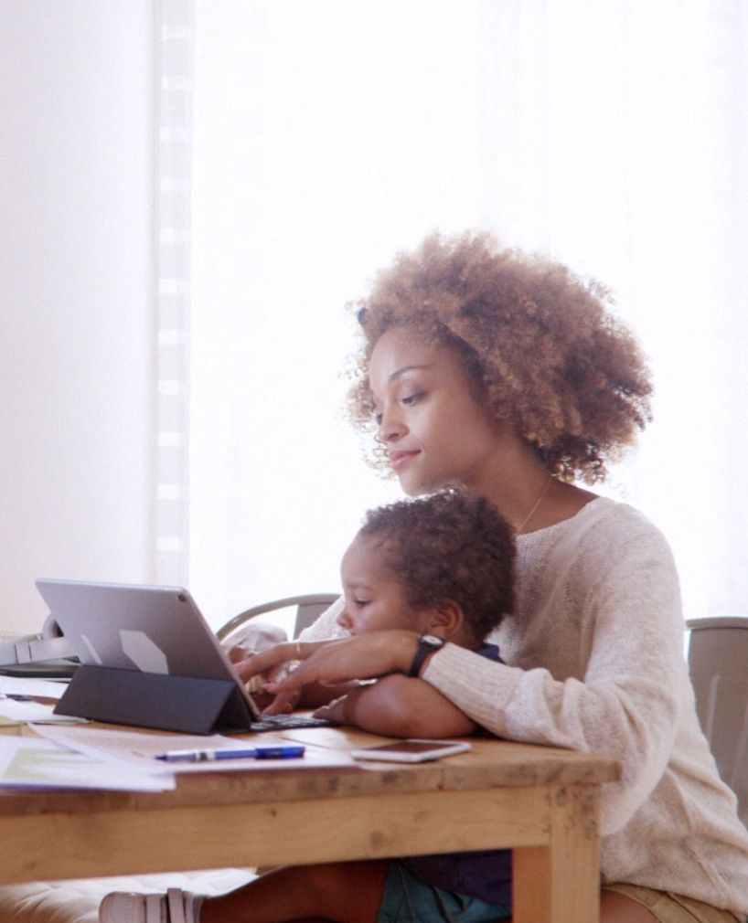 Woman holding child while working on her tablet
